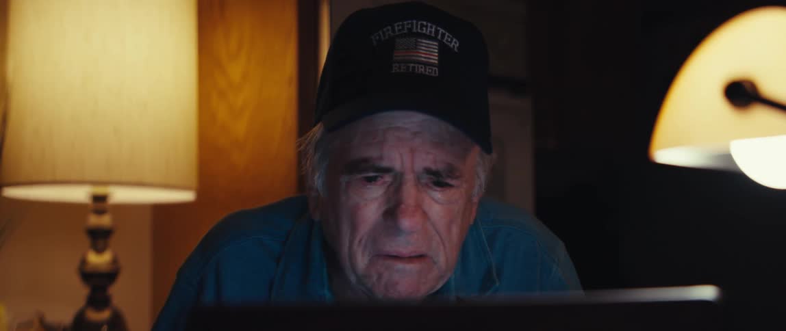 Close-up of an elderly retired firefighter becoming emotional and crying while looking at a computer screen in a dark room