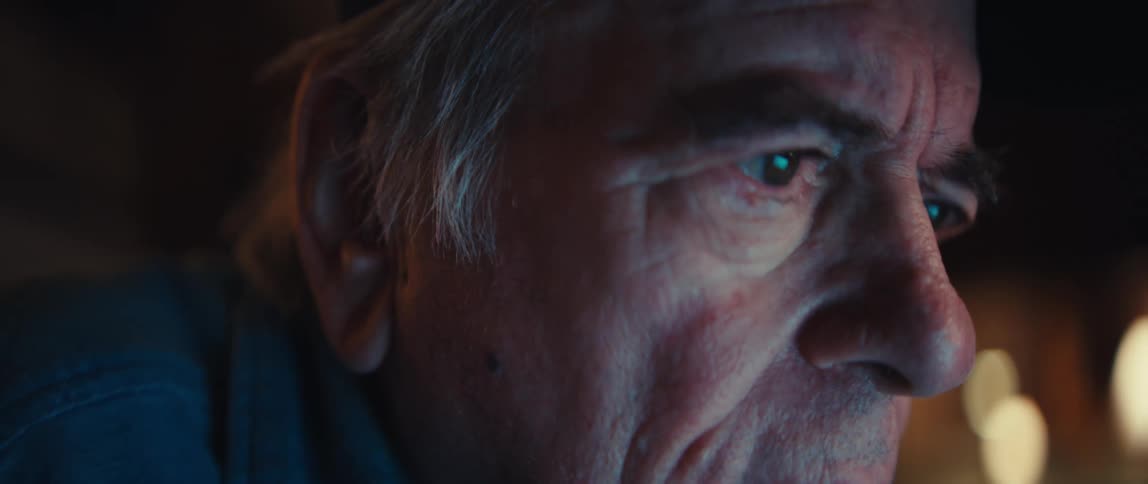An extreme close-up shot of an elderly man's face as the camera slowly pulls focus on his eye, reflecting the glow of a screen