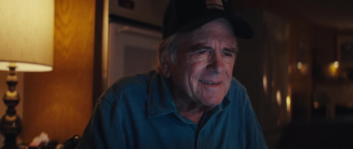 A retired firefighter smiles warmly as he looks at his computer screen in a warmly lit room