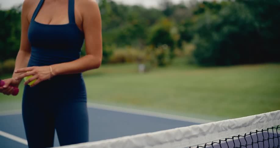Slow motion shot of a fit woman holding a pickleball paddle and ball at the net on an outdoor court
