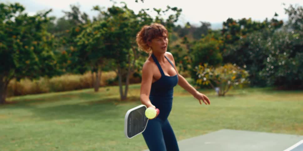 A focused woman hits a pickleball with her paddle in a dynamic super slow-motion shot on an outdoor court