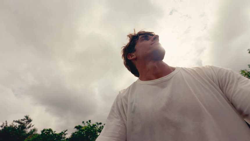 Low angle selfie-style slow-motion shot of a young man on a tennis court looking up triumphantly at the sky