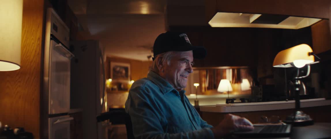 A happy elderly man in a wheelchair enjoys using his laptop computer at home in the evening