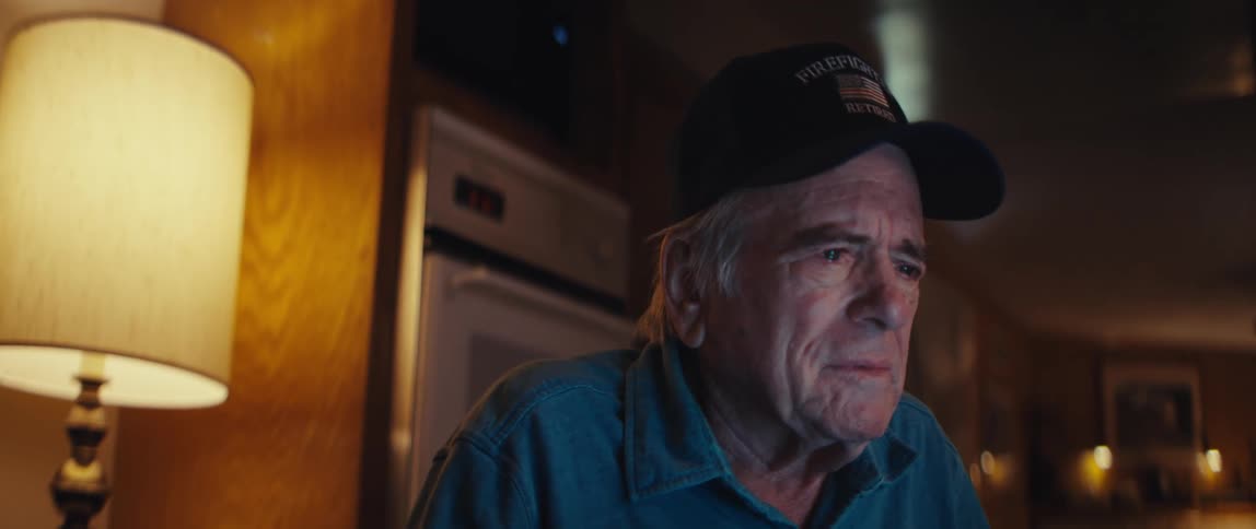 A retired firefighter gets emotional and tears up while watching a screen in his home at night