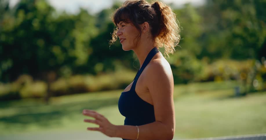 An athletic woman smiles as she swings her pickleball paddle in slow motion on a beautiful sunny day