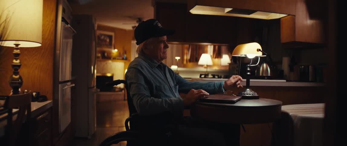 After finishing on his laptop, a pensive senior man in a wheelchair sits alone in the quiet solitude of his home at night