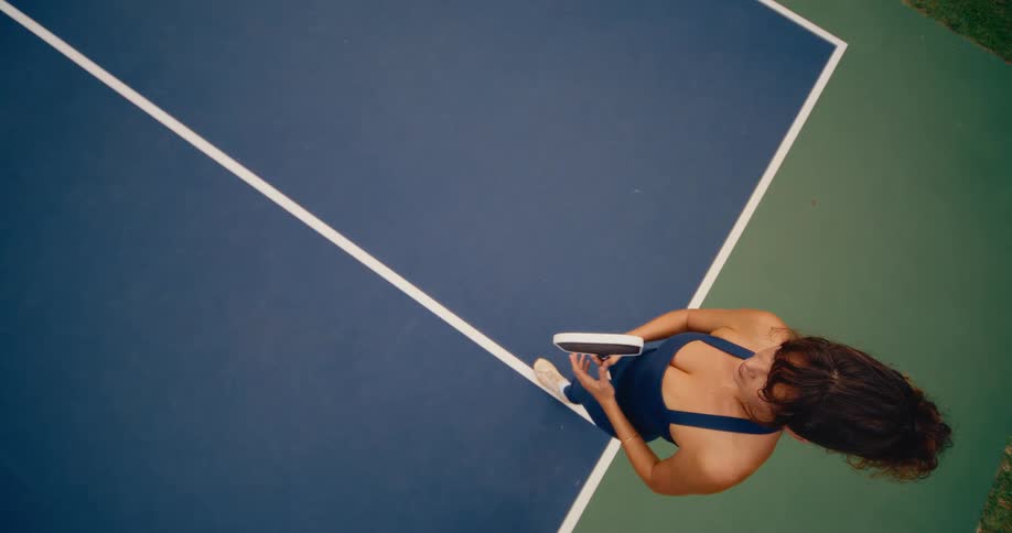 High-angle slow motion shot of a woman in an athletic outfit practicing her pickleball serve on a blue and green court