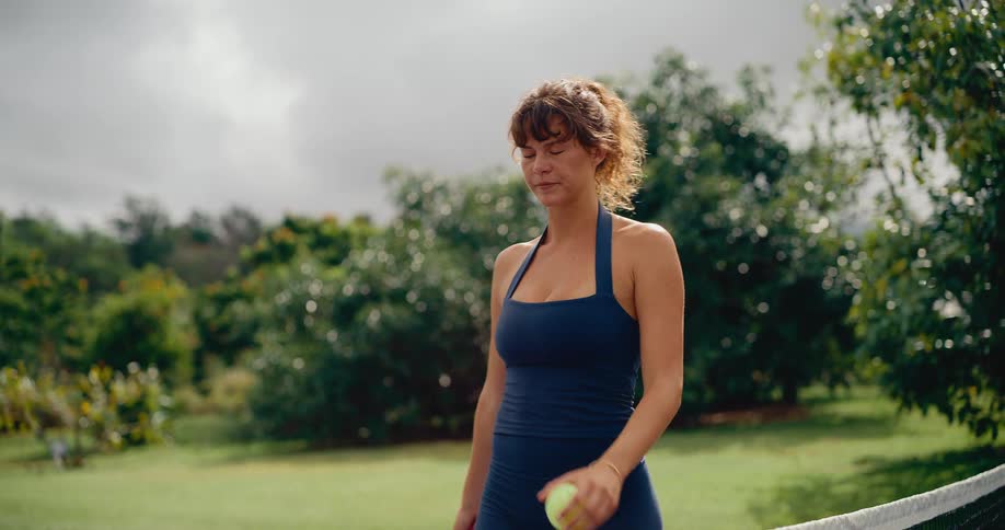 A woman in athletic attire walks in slow motion on a pickleball court, holding her paddle and ball