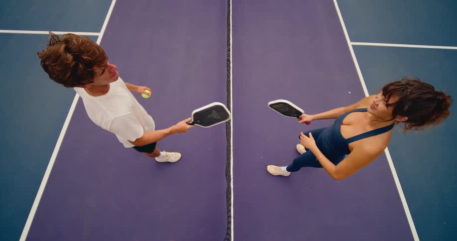 Good sportsmanship on the pickleball court as a man and woman tap paddles over the net in a slow-motion overhead view