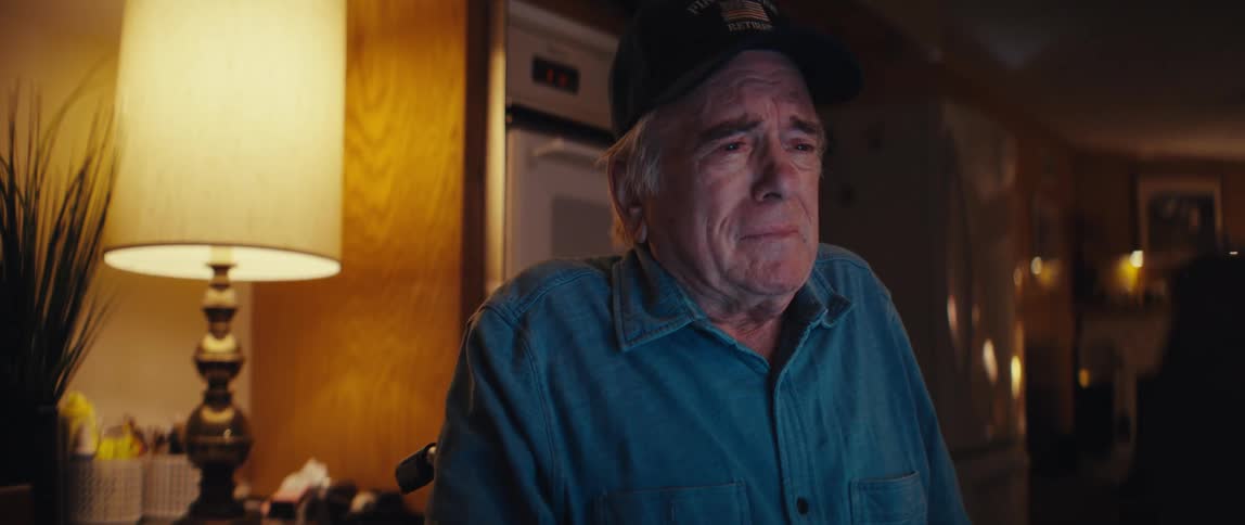 A close-up of an emotional elderly retired firefighter tearing up while looking at his computer screen in a dimly lit room