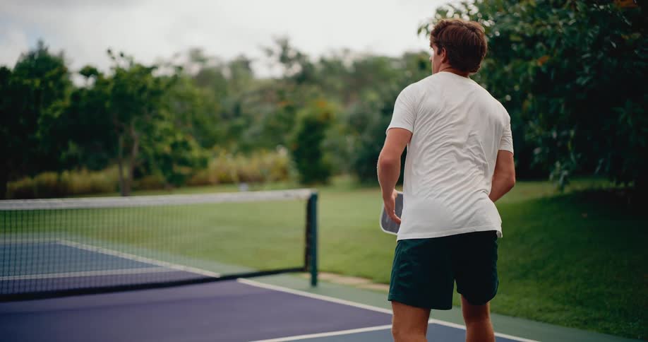 Slow motion shot of a man from behind returning a shot during a game of pickleball