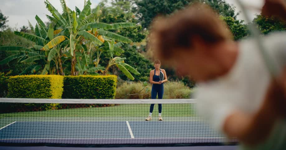 A man and woman rally back and forth while playing pickleball on a beautiful outdoor court in slow motion