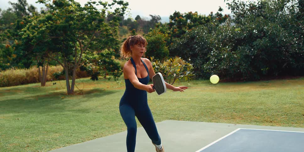 Super slow motion shot of a focused woman hitting a pickleball during a game on an outdoor court