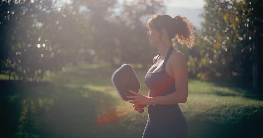 A woman in athletic wear hits a pickleball with a forehand swing in slow motion on a beautiful sunny day
