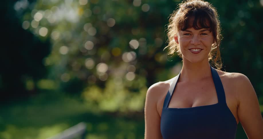 Slow motion close up of a beautiful and athletic woman holding a pickleball and paddle as she smiles and looks into the camera on a sunny day