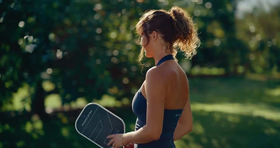 Slow motion shot of a smiling woman in athletic wear hitting a pickleball with her paddle in a sunny park