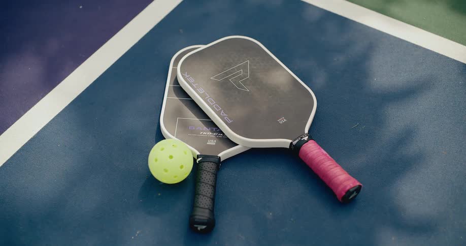 Two pickleball paddles and a yellow ball rest on the blue surface of a court