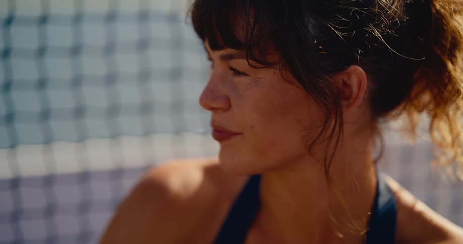 Close-up slow-motion shot of a smiling female athlete with freckles relaxing in the sunshine next to a net