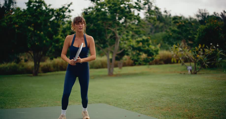 Focused woman in athletic wear hits a pickleball with a forehand stroke in a beautiful park setting