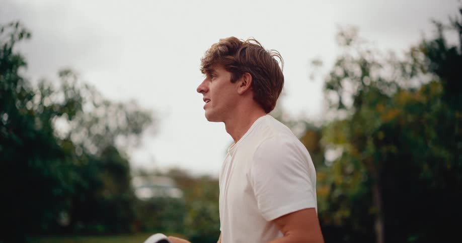 A focused athlete in a white shirt and green shorts plays a game of pickleball on an outdoor court, hitting the ball in slow motion