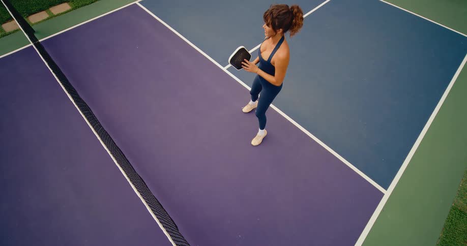 High-angle slow-motion shot of a woman practicing her dink shot on a purple and blue pickleball court
