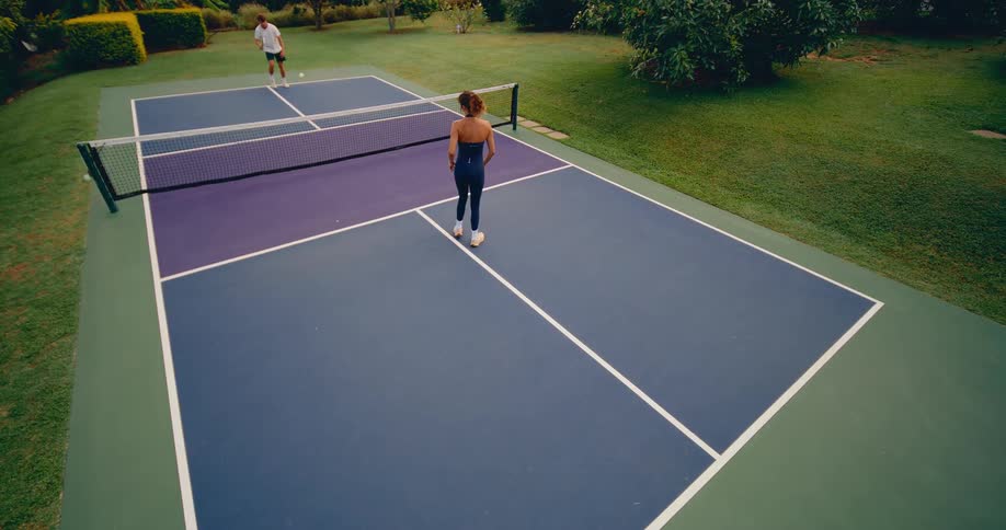 A man and woman exchange shots during a slow-motion game of pickleball on a vibrant outdoor court