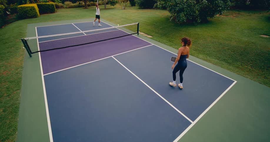 High-angle view of a man and woman engaged in a slow-motion rally on an outdoor pickleball court
