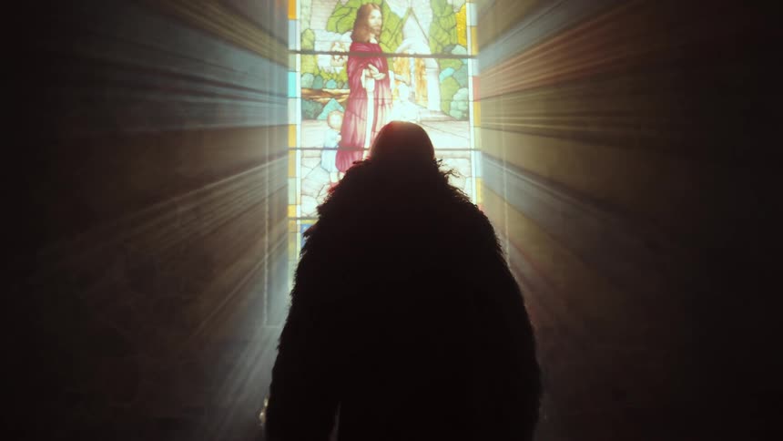 A silhouetted figure in a heavy fur coat slowly approaches a stained glass window of Jesus in a dark church, illuminated by dramatic heavenly light rays
