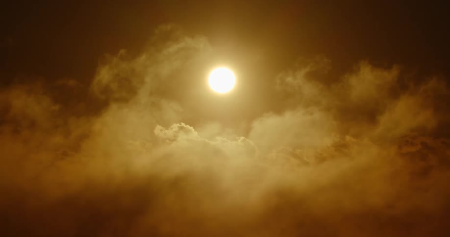 The bright sun shines brilliantly through a hazy, slow-moving sea of golden clouds