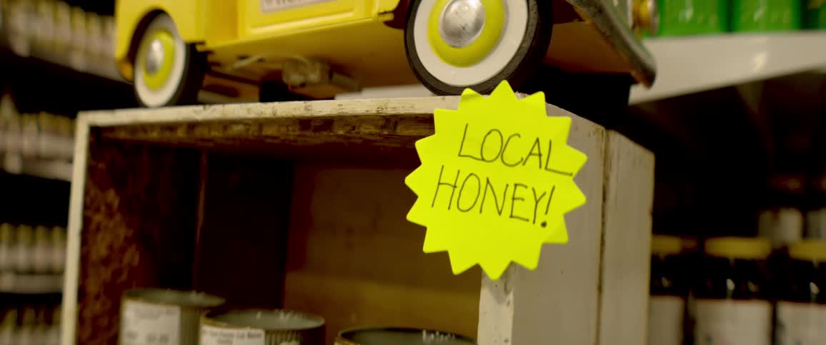 A vibrant yellow sign promoting local honey sits on a rustic wooden shelf in a shop
