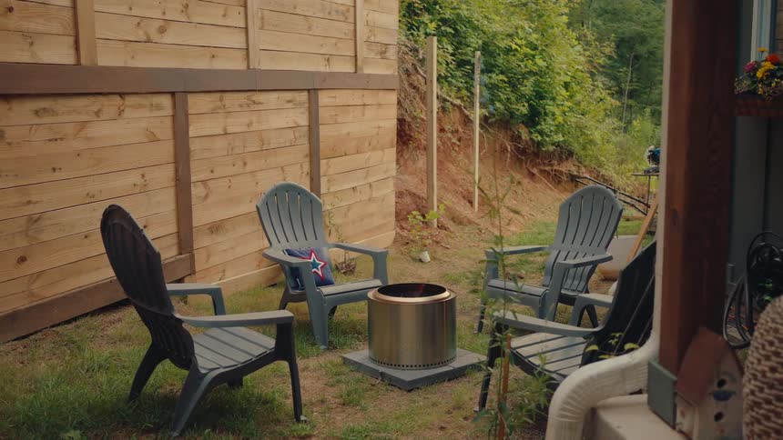 A modern stainless steel fire pit burns brightly in a cozy backyard setting surrounded by grey Adirondack chairs