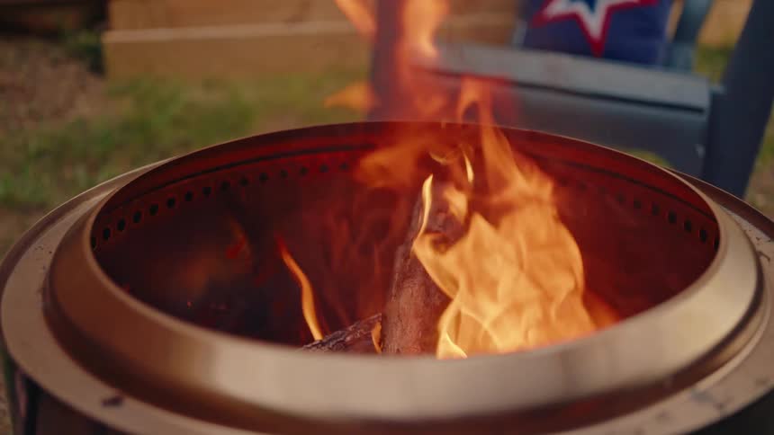 Slow motion close-up of a cozy backyard bonfire burning brightly in a modern stainless steel fire pit