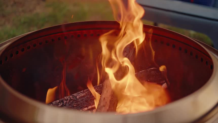 A close-up slow-motion shot of a vibrant fire burning inside a modern stainless steel fire pit in a backyard