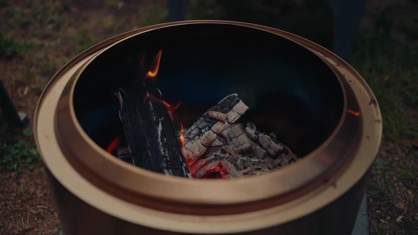 A close-up view of a modern smokeless fire pit with gently burning logs and glowing embers