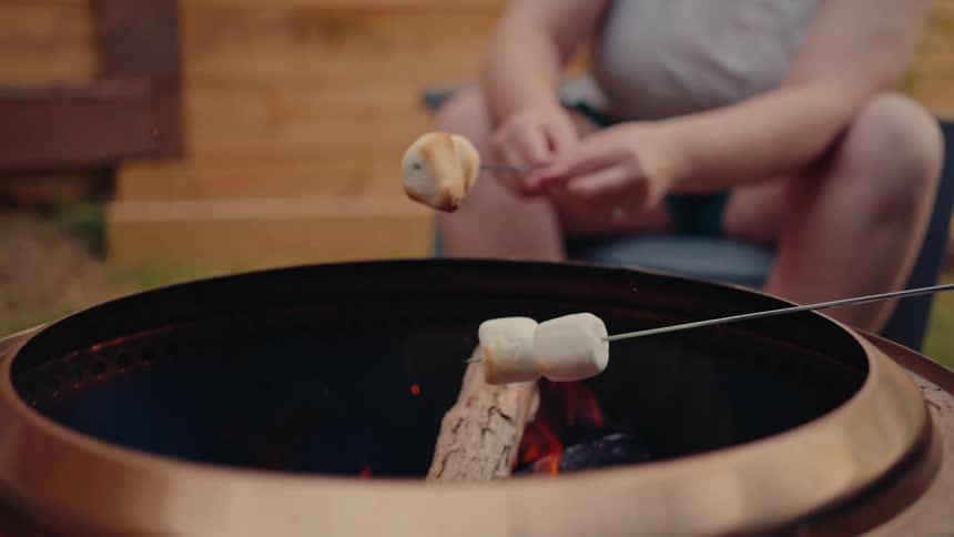 A close-up slow motion shot shows marshmallows being slowly roasted over a backyard fire pit