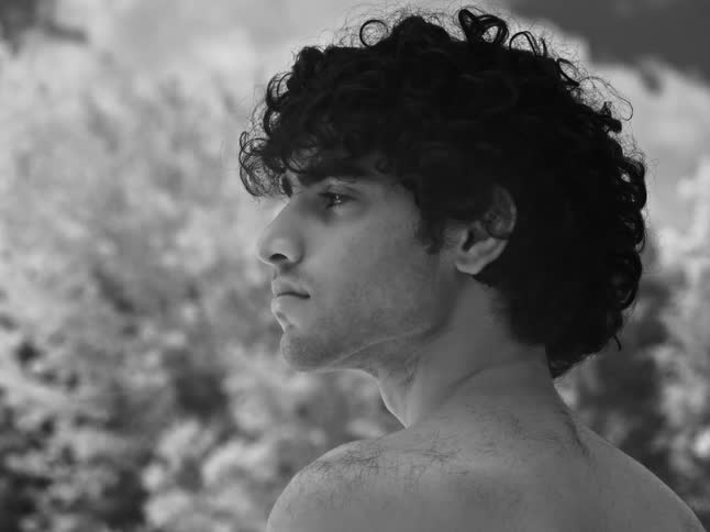 A black and white cinemagraph shows a still portrait of a pensive young man with a subtle shimmering light effect