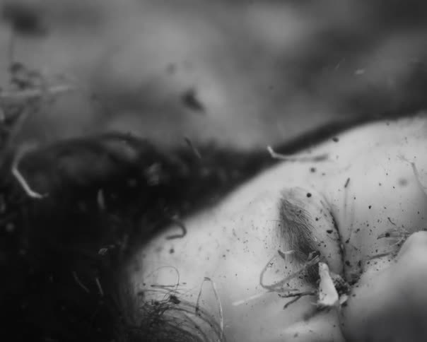 A haunting black and white close-up reveals a person's face as dirt and debris lift away in reverse motion