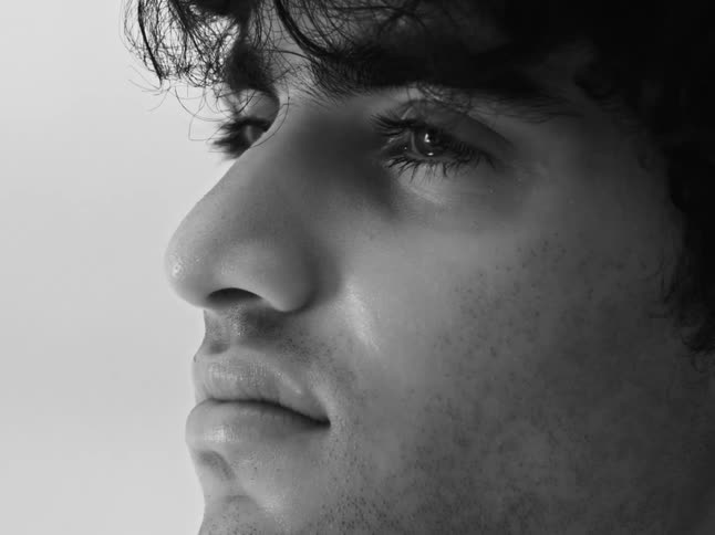 A dramatic black and white close-up profile shot of a pensive young man with dark curly hair
