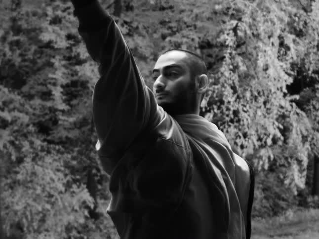 Slow motion black and white footage shows a serious man turning his head in a windy forest