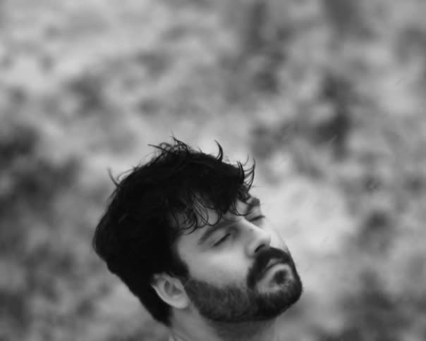A bearded man closes his eyes and lets the rain fall on his face in a black and white close-up