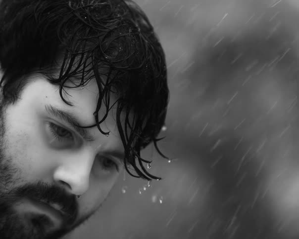 Dramatic black and white close-up of a sad bearded man with wet hair standing in the pouring rain