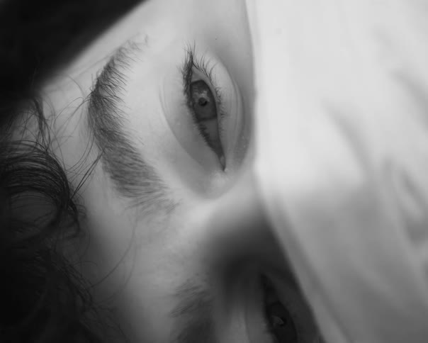 An intimate black and white vertical close-up captures the subtle, contemplative movement of a person's eye