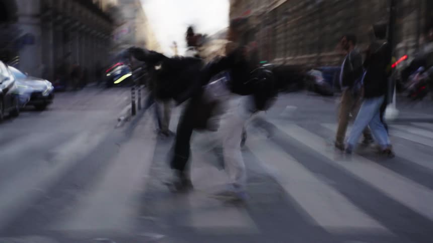 An abstract, motion-blurred view of pedestrians and traffic moving quickly through a busy city crosswalk