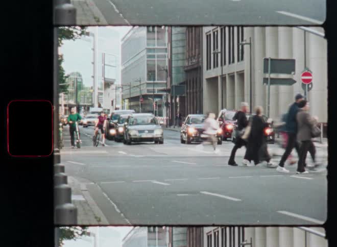 Authentic 8mm film footage of people and cyclists crossing a busy street in a modern city with a light leak effect