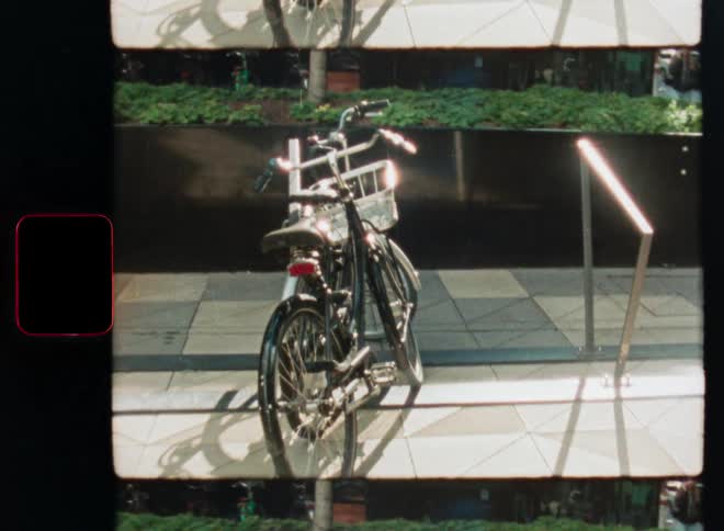 A retro Super 8mm film scan shows a bicycle parked on a city sidewalk with light leaks at the end