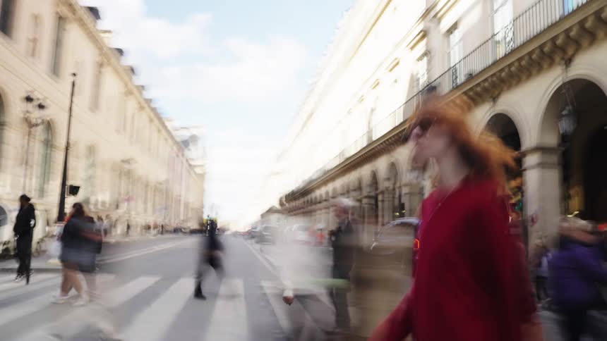 A woman stands still in a red sweater as the busy Parisian city street blurs past her in a fast-motion time-lapse