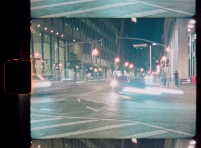 A long exposure timelapse on vintage 8mm film captures cars creating light streaks on a busy city street at night