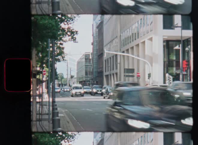 A vintage film strip aesthetic captures the motion of cars driving through a busy city intersection