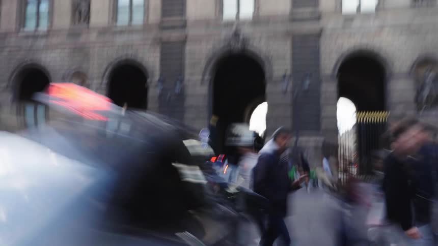 A woman in a red sweater walks calmly across a busy street as the surrounding city blurs into motion in a slow-shutter speed shot