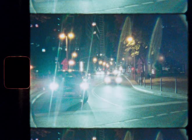 Nighttime traffic creates beautiful light trails in a grainy, vintage film time-lapse of a city intersection